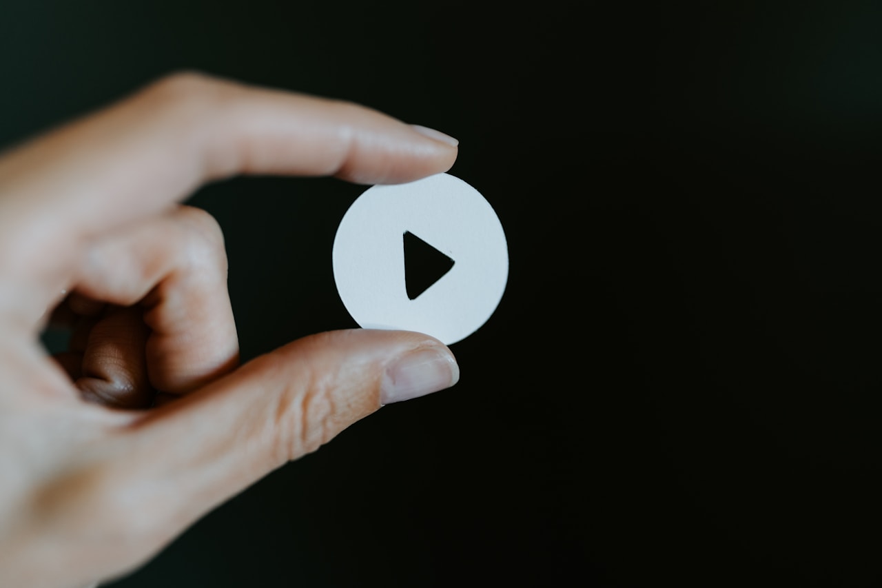 Hand holding a white paper cut-out of a video play button